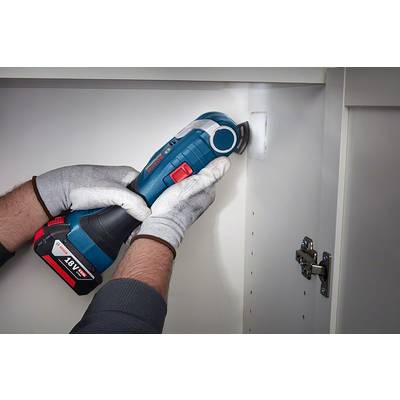Eine Person arbeitet mit einem blauen, akkubetriebenen Multitool in einem weißen Schrank, trägt graue Handschuhe.