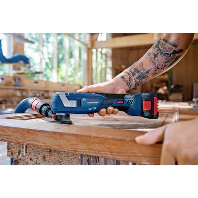 Person verwendet ein elektrisches Multifunktionswerkzeug zum Schleifen von Holz in einer Werkstatt. Tattoos sichtbar.