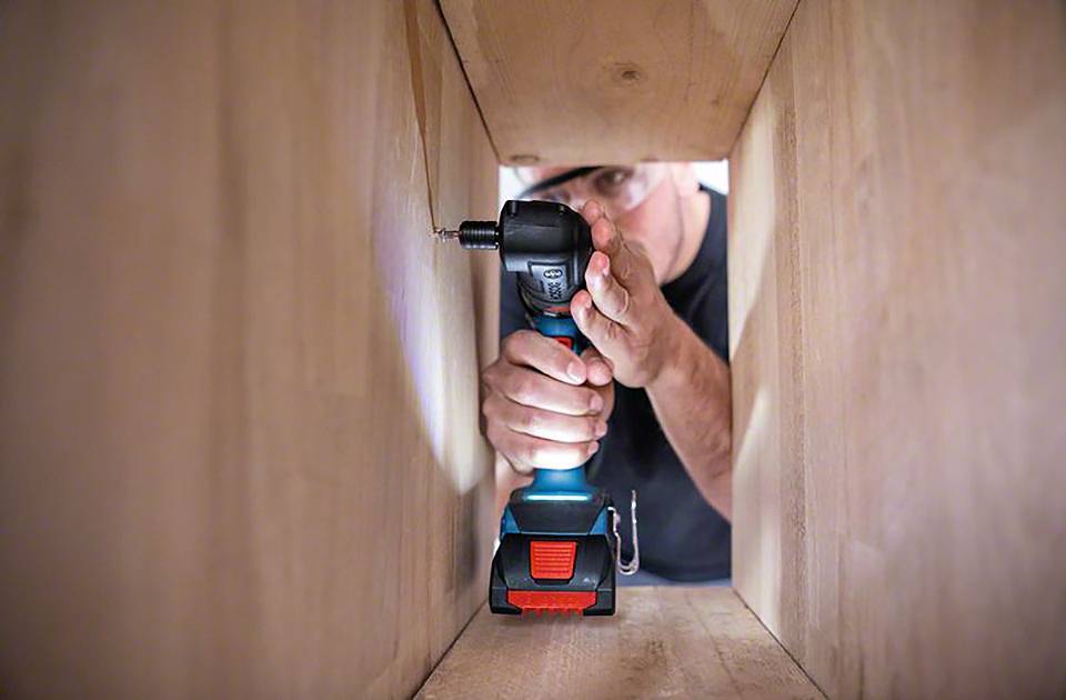 Eine Person arbeitet innerhalb eines Holzrahmens und benutzt einen Akkuschrauber, um eine Schraube anzubringen.