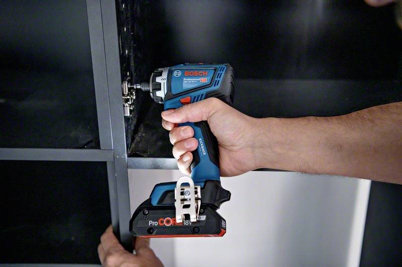 Person schraubt mit einem Akkuschrauber ein Scharnier an einen Schrank. Der Akkuschrauber ist blau und wird mit beiden Händen gehalten.