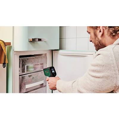 Ein Mann benutzt ein Infrarotthermometer, um die Temperatur des Gefrierschranks zu messen. Der Gefrierschrank ist geöffnet und vereist.