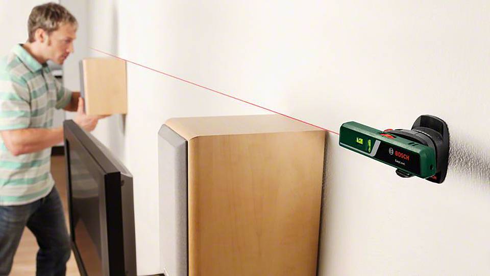 Ein Mann verwendet ein Laser-Nivelliergerät an der Wand, um ein Holzregal gerade auszurichten.