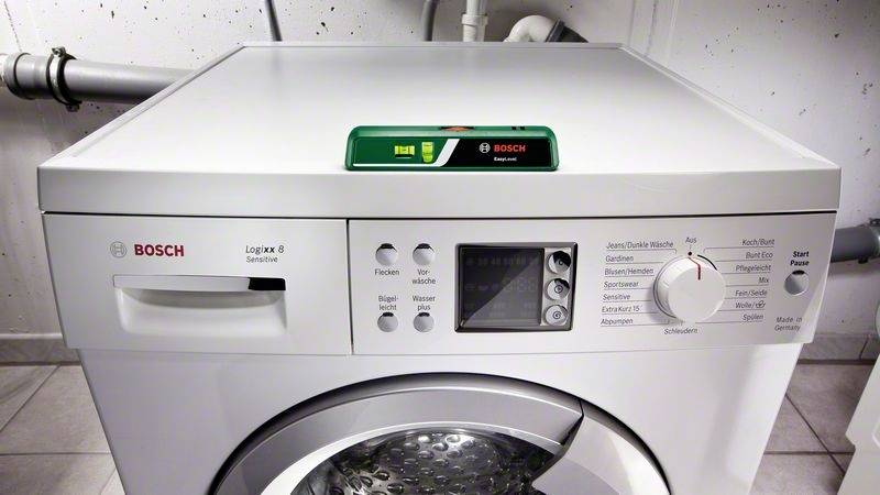 Die Abbildung zeigt eine weiße Bosch Waschmaschine von vorne mit einem grünen Wasserwaage auf der Oberseite.