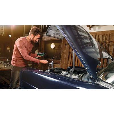 Ein Mann prüft mit einem Messgerät den Motor eines Autos, das in einer Werkstatt steht. Die Motorhaube ist geöffnet, das Auto steht still.