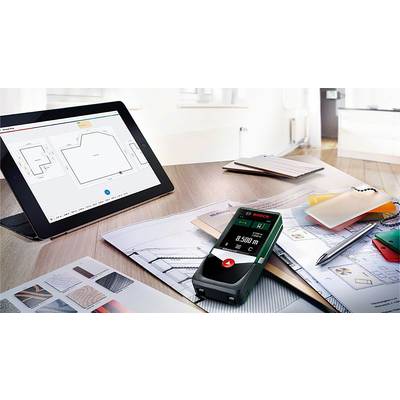 Ein Tablet zeigt einen Grundriss. Daneben liegen ein Laserentfernungsmesser, Papierpläne und Farbproben auf einem Tisch in einem modernen Büro.