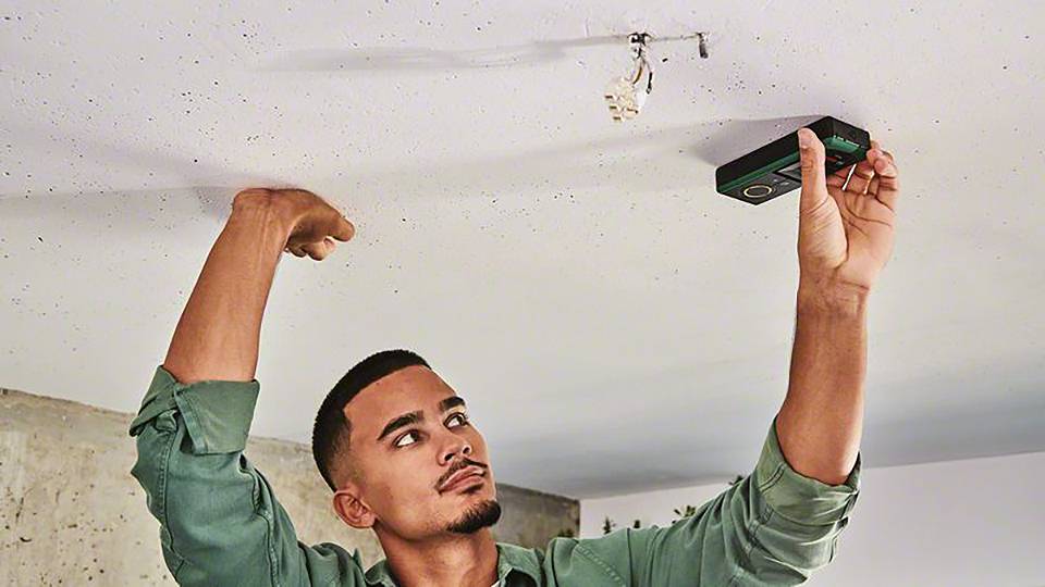 Ein Mann installiert eine Lampe an der Decke und benutzt ein Werkzeug zum Ausrichten.