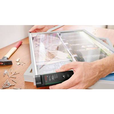 Eine Person richtet einen Rahmen mit einem digitalen Winkelmesser auf einem Tisch aus. Hammer und Nägel liegen daneben.