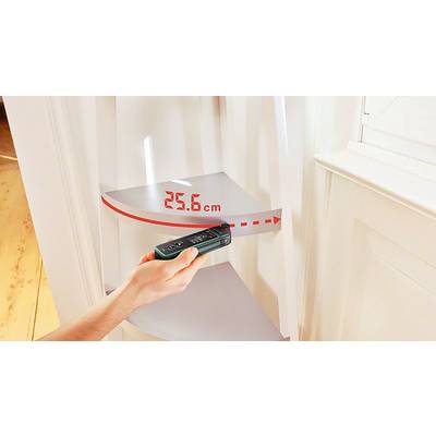 Eine Hand hält ein digitales Messgerät in einem Raum und misst eine Distanz von 25,6 cm an einer weißen Wand.
