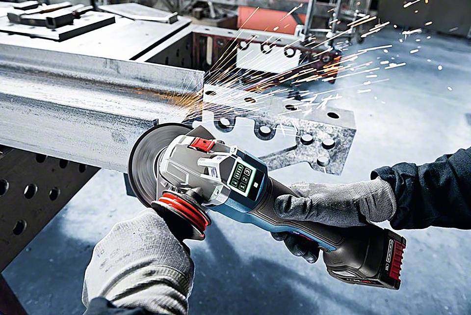 Ein Arbeiter schleift ein Metallstück mit einem Winkelschleifer. Funken fliegen vom Kontaktpunkt ab. Der Arbeiter trägt Schutzhandschuhe.