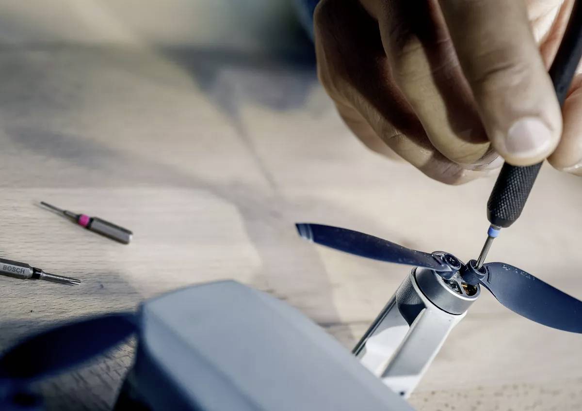 Hand montiert Rotorblätter an einer Drohne auf einem Tisch, mit Schraubendreher und anderen Werkzeugen in der Nähe.