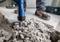 Arbeiter benutzt einen Bohrhammer, um Beton zu brechen. Nahaufnahme zeigt Staub und Schutt auf dem Boden, Schuh des Arbeiters sichtbar.