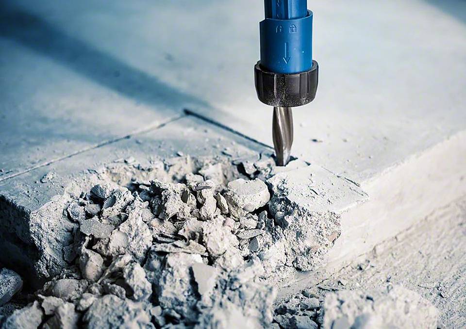 'Bohrmaschine bearbeitet Betonplatte mit Staub und Trümmern drumherum.'