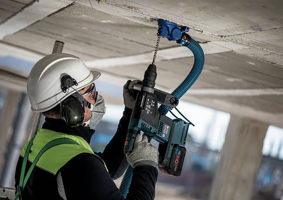 Ein Bauarbeiter mit Schutzkleidung bohrt mit einem Elektrowerkzeug ein Loch in die Decke.
