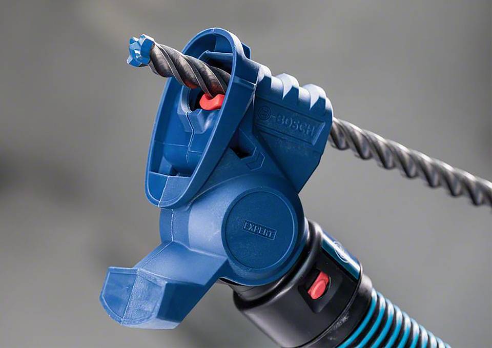 Blaue Bohrmaschine mit Befestigung, die einen Bohrer hält. Sie ist in Aktion und zeigt den Bohraufsatz. Hintergrund unscharf.