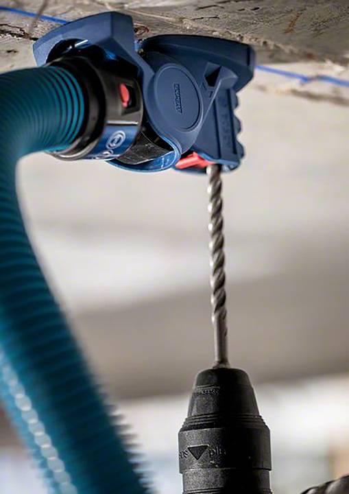 Bohrmaschine mit Staubabsaugungssystem an Decke im Einsatz. Drill und Staubsauger sind verbunden, um Staub zu minimieren.