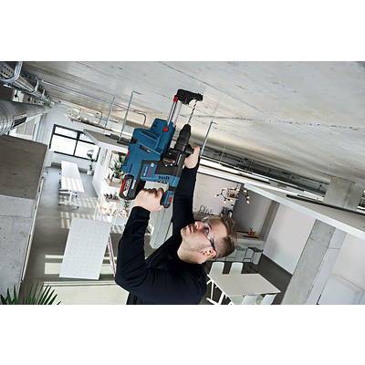 Eine Person in einer industriellen Umgebung bohrt mit einer großen, blauen Bohrmaschine in eine Betondecke. Im Hintergrund sind moderne Möbel.