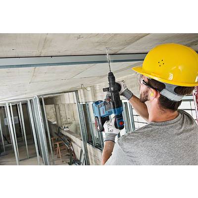 Ein Bauarbeiter mit Schutzhelm und Gehörschutz bohrt mit einer elektrischen Bohrmaschine in eine Decke.