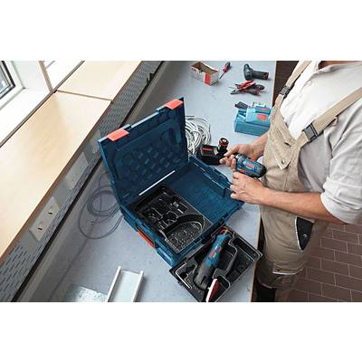 Eine Person steht an einer Werkbank und verwendet Elektrowerkzeuge aus einem geöffneten Koffer. Zubehörteile sind im Hintergrund sichtbar.
