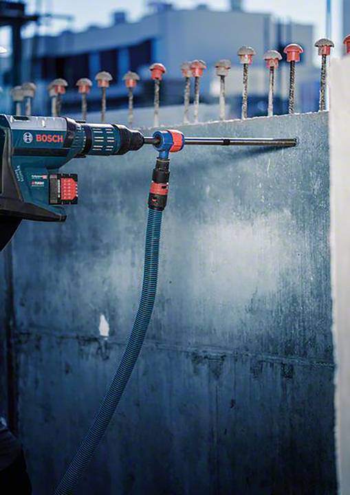 'Nahaufnahme eines Bauarbeiters, der mit einem Bohrhammer von Bosch eine Betonwand bearbeitet. Im Hintergrund sind Bewehrungsstäbe zu sehen.'