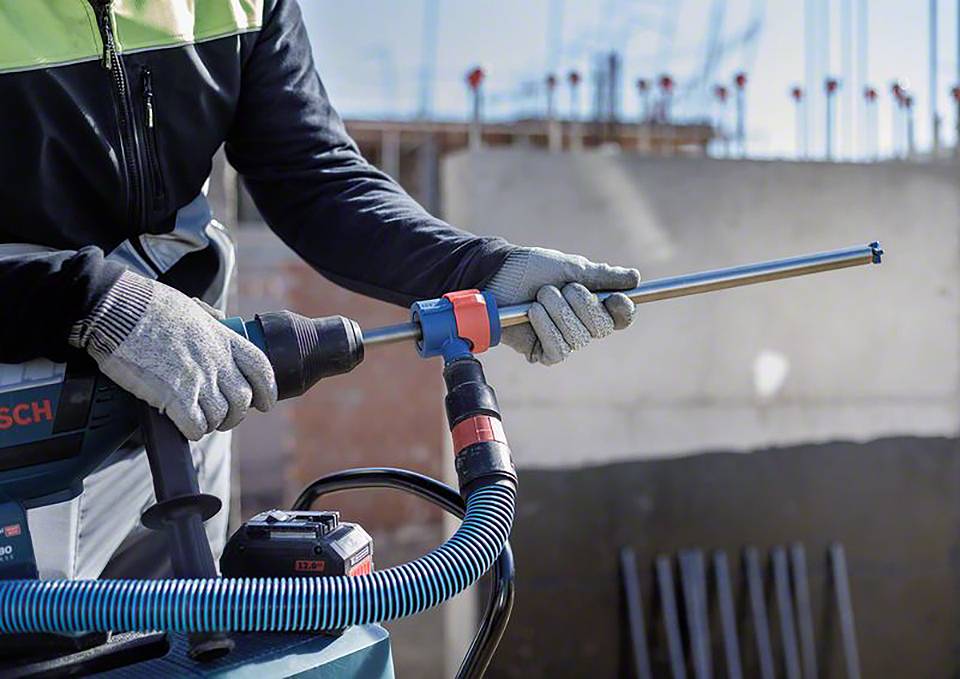 Person verwendet eine elektrische Bohrmaschine mit Staubsaugeraufsatz auf einer Baustelle, um in eine Betonwand zu bohren.