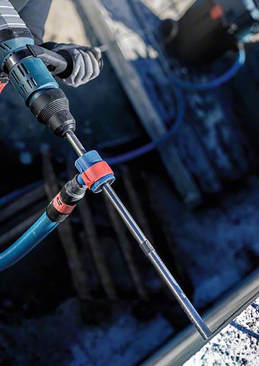 Eine Person bohrt mit einem elektrischen Bohrhammer in Beton, Hände in Handschuhen. Fokus auf Werkzeug und Bohrfläche, blaue Umgebung.