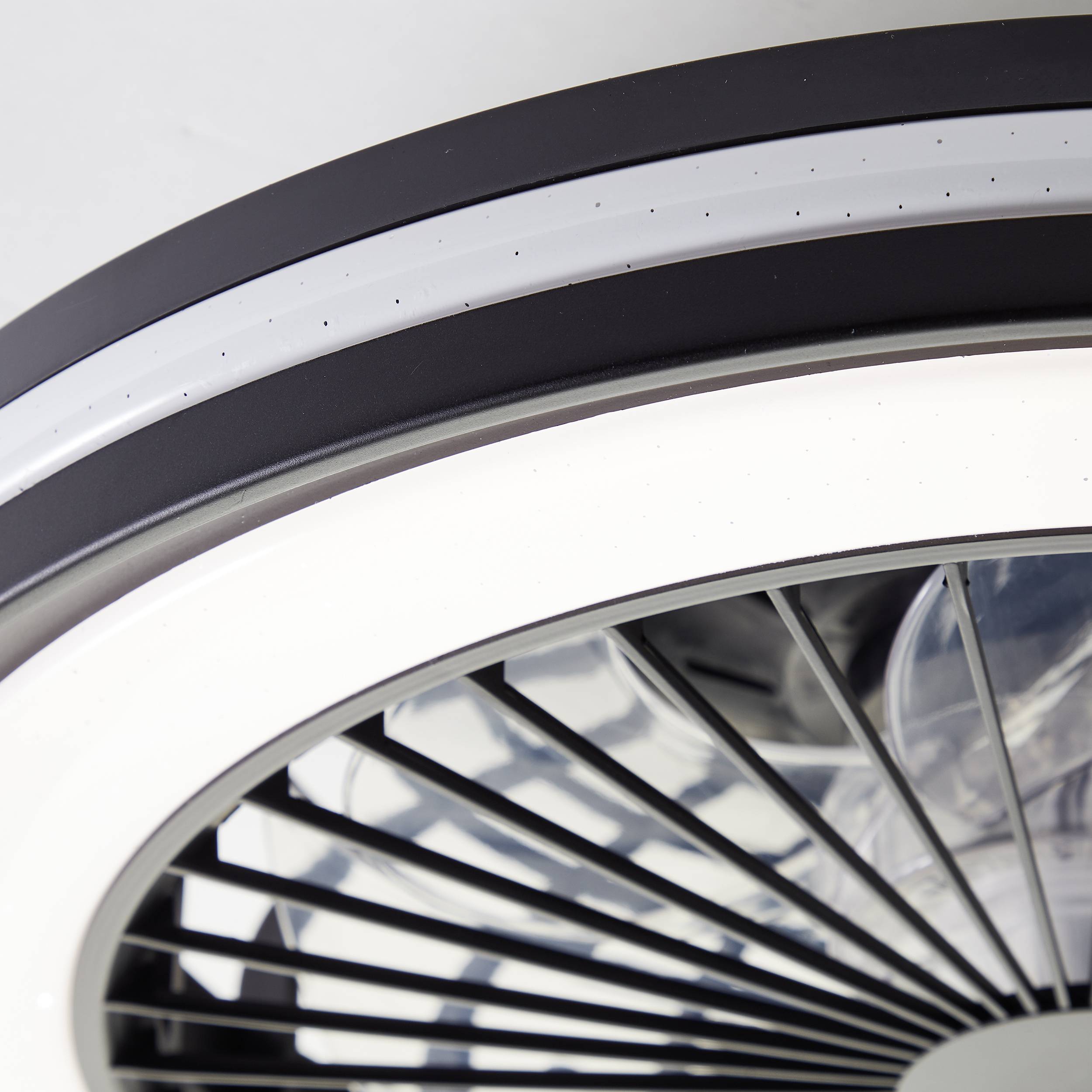 Nahaufnahme eines modernen Deckenventilators mit runden, schwarzen und grauen Elementen und weißen Lichtelementen.