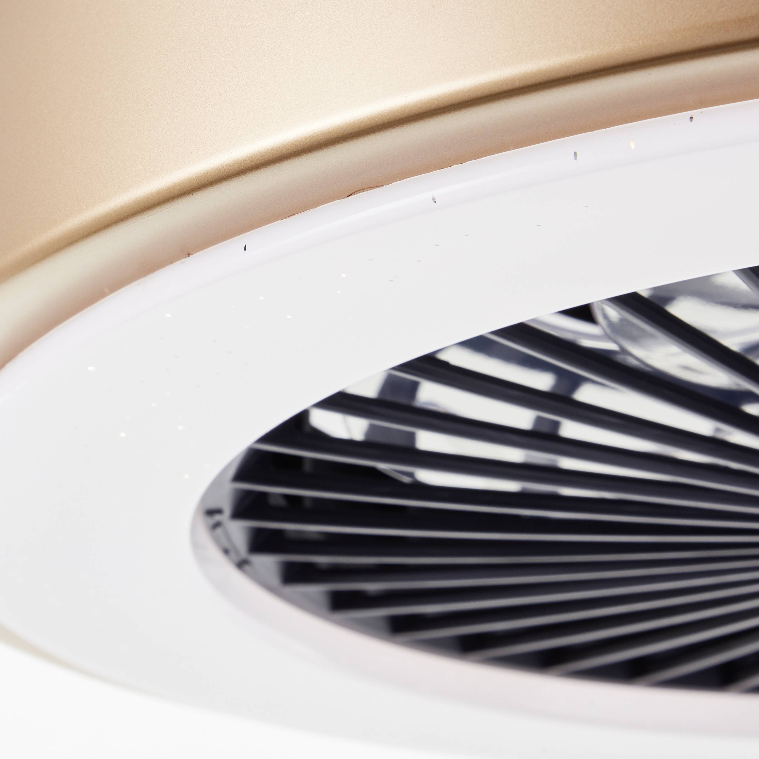 Ein moderner Deckenventilator mit glänzendem goldfarbenem Gehäuse und klaren Lüfterblättern dreht sich in einem gut beleuchteten Raum.