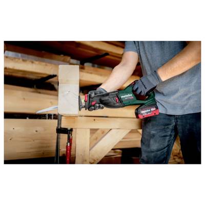 Eine Person verwendet eine Säbelsäge, um ein Stück Holz zu schneiden, das an einer Werkbank in einer Schreinerei eingespannt ist.