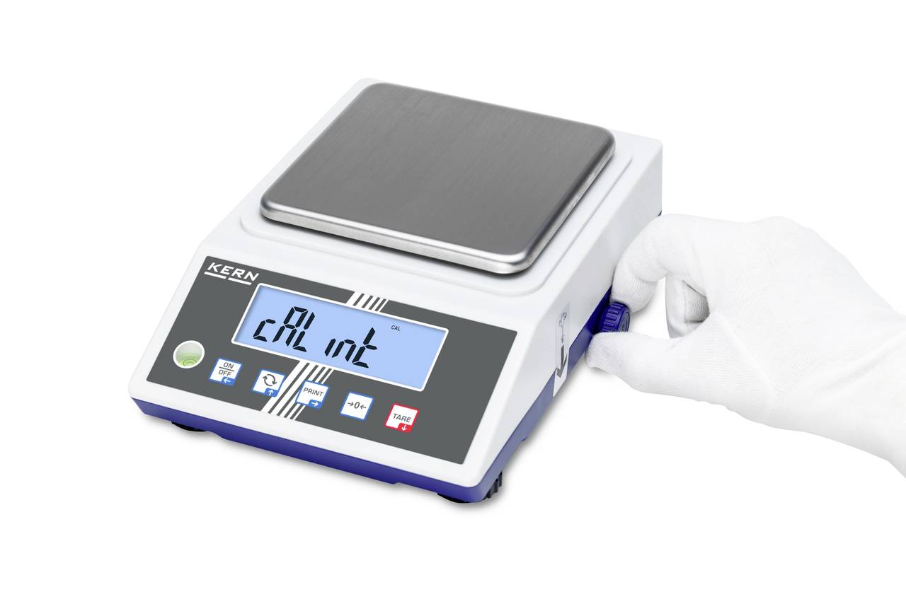 Eine digitale Laborwaage mit einem LCD-Display zeigt 'CAL int' an. Eine behandschuhte Hand dreht einen blauen Knopf an der Seite.