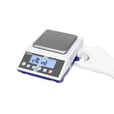 Eine elektrische Präzisionswaage mit einem digitalen Display, auf dem 'cAL int' angezeigt wird. Eine Hand dreht einen Einstellknopf.