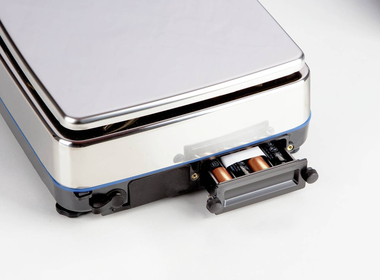 Digitalwaage mit herausgezogenem Batteriefach, das vier AA-Batterien zeigt.