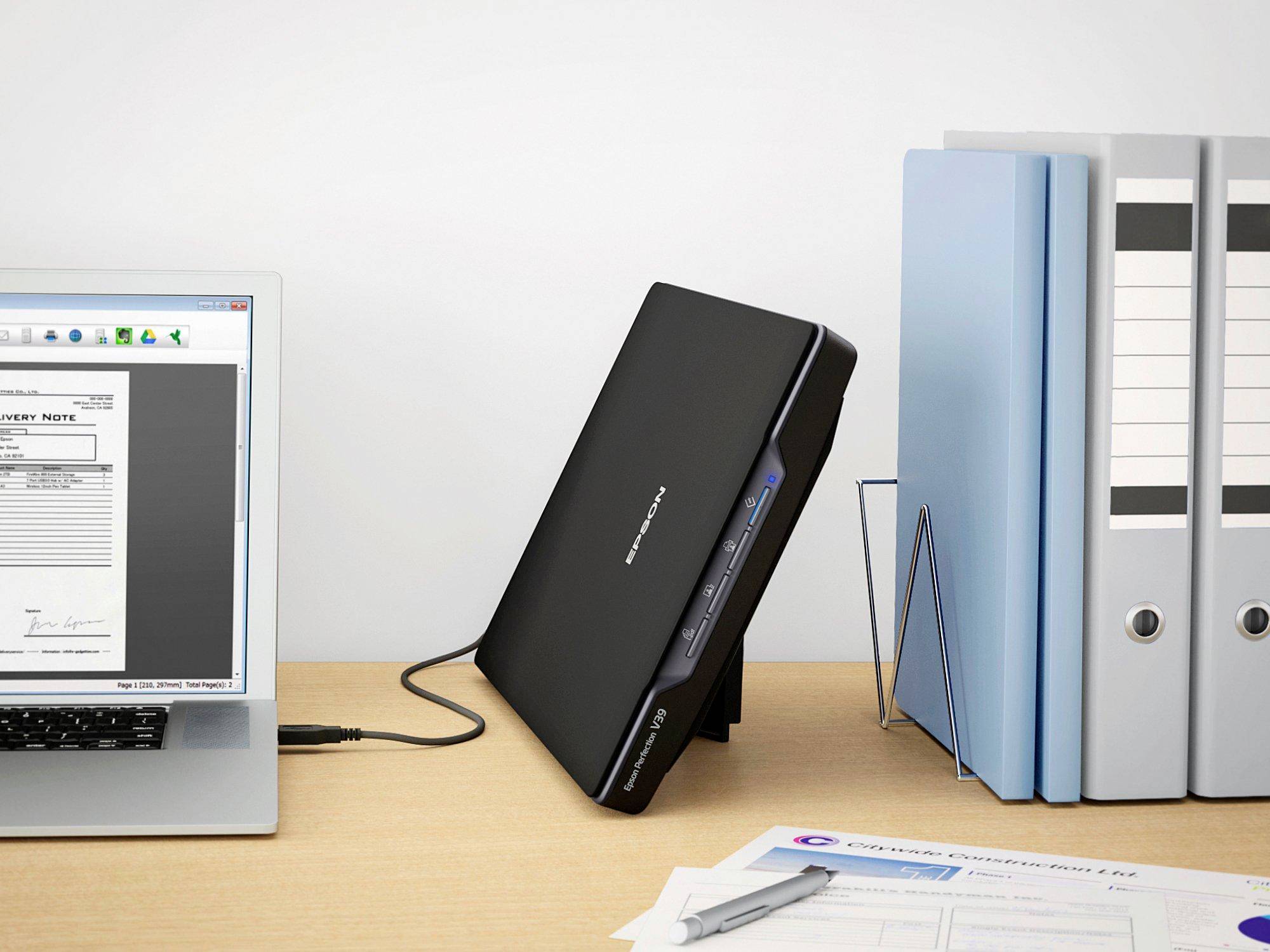 Ein Scanner scannt ein Dokument auf einem Schreibtisch. Der Laptop zeigt das gescannte Dokument an. Ordner und Papiere liegen daneben.