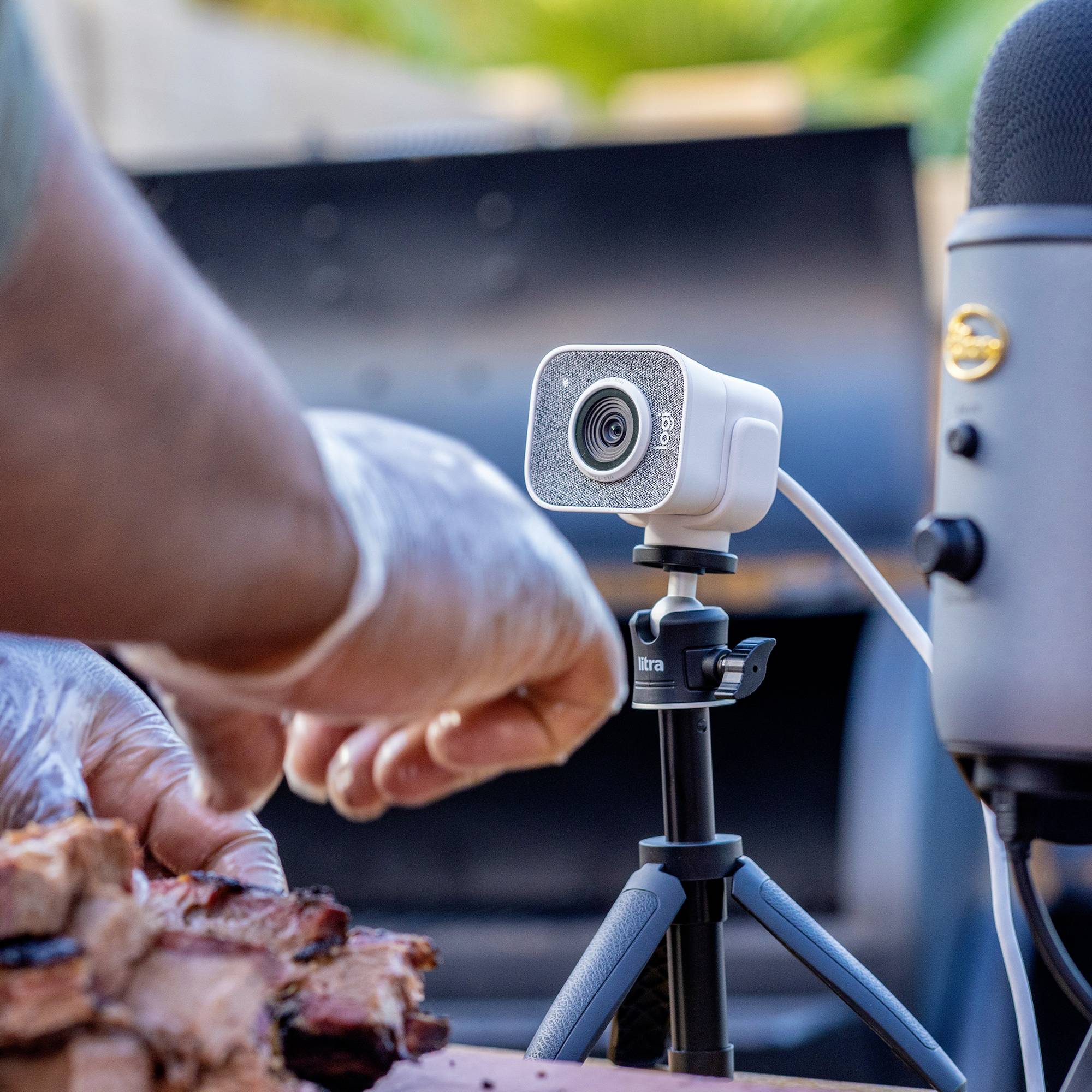 Person schneidet Fleisch bei Grillen; im Vordergrund Stücke Fleisch, im Hintergrund auf Stativ montierte Kamera.