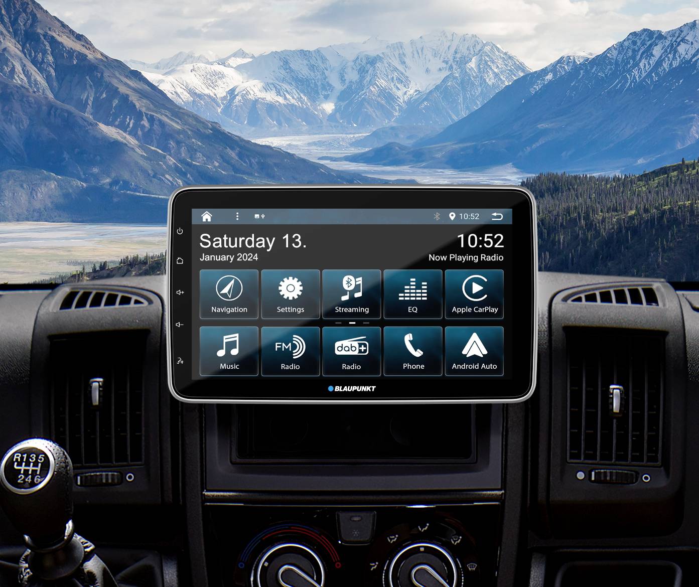 Das Bild zeigt das Innenleben eines Autos mit einem modernen Navigationssystem auf dem Armaturenbrett und Berglandschaft im Hintergrund.