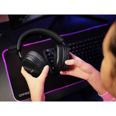 Eine Person hält ein schwarzes Headset vor einem beleuchteten Desktop-Computer mit Tastatur. Die Szene deutet auf eine Spielsituation hin.