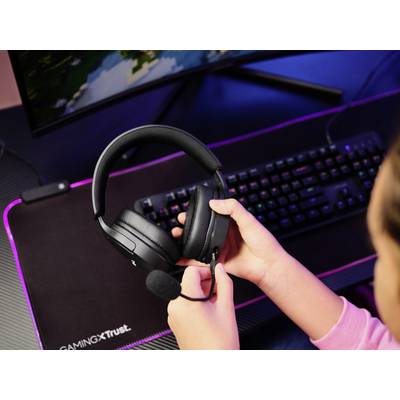 Eine Person hält ein Headset mit Mikrofon vor einem Computerbildschirm und einer beleuchteten Tastatur. Es scheint eine Gaming-Szene zu sein.