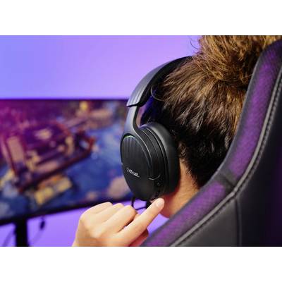 Eine Person sitzt vor einem großen Bildschirm und spielt ein Videospiel. Sie trägt ein Headset und hat eine Hand am Ohrhörer.