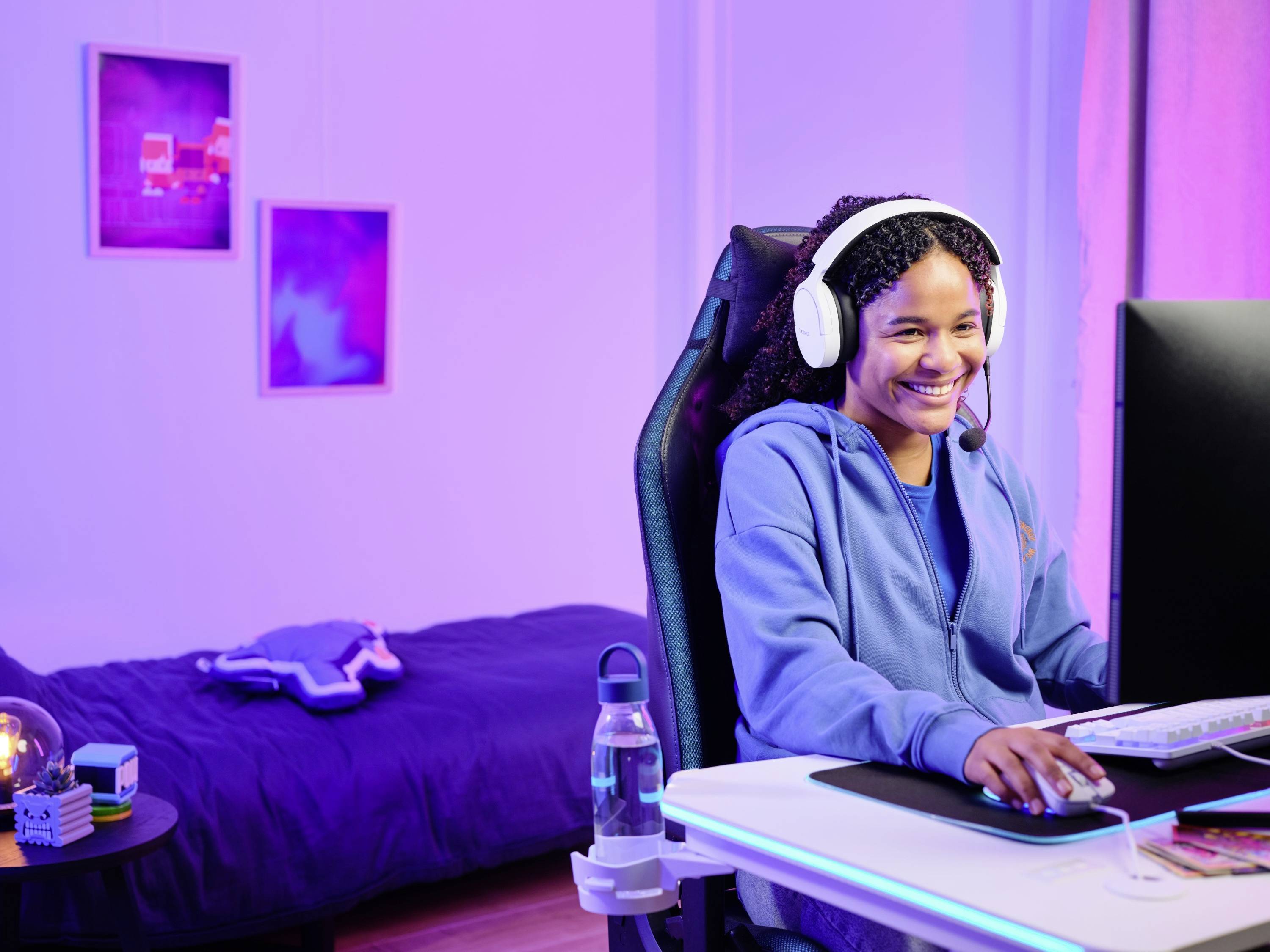 Eine Person mit Kopfhörern und Mikrofon spielt auf einem Computer in einem Schlafzimmer mit stimmungsvoller Beleuchtung.