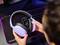 Eine Person hält ein kabelloses Headset über einem Schreibtisch mit Mauspad und beleuchteter Tastatur.