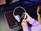 Eine Person hält ein weißes Gaming-Headset über einem Computer mit sichtbarer Tastatur und Mauspad auf einem Tisch.