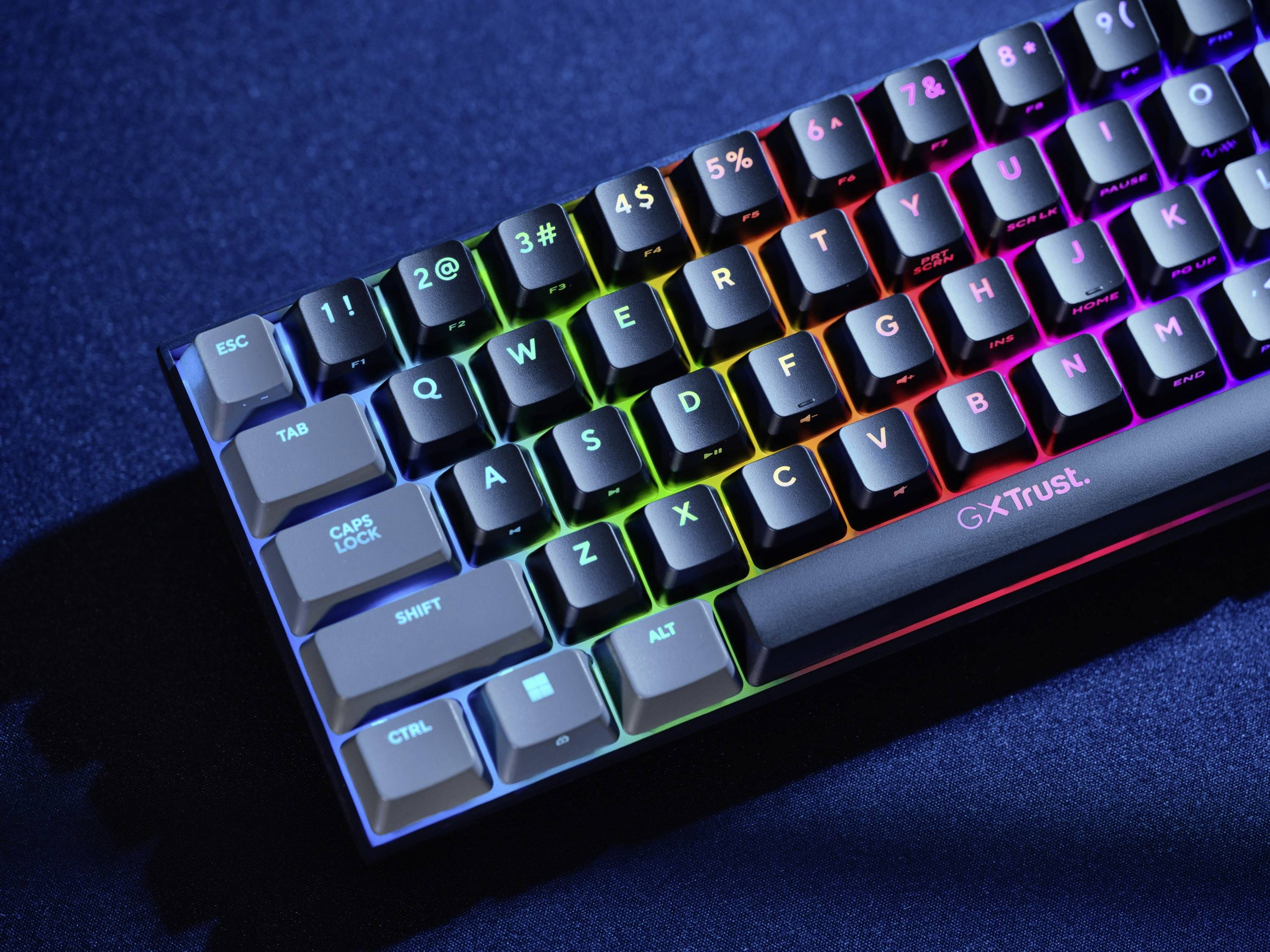 Beleuchtete Gaming-Tastatur mit Regenbogen-LEDs. Sichtbar sind die Tasten von ESC bis ALT sowie der Name 'Trust'.