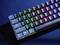 Beleuchtete Gaming-Tastatur mit Regenbogen-LEDs. Sichtbar sind die Tasten von ESC bis ALT sowie der Name 'Trust'.