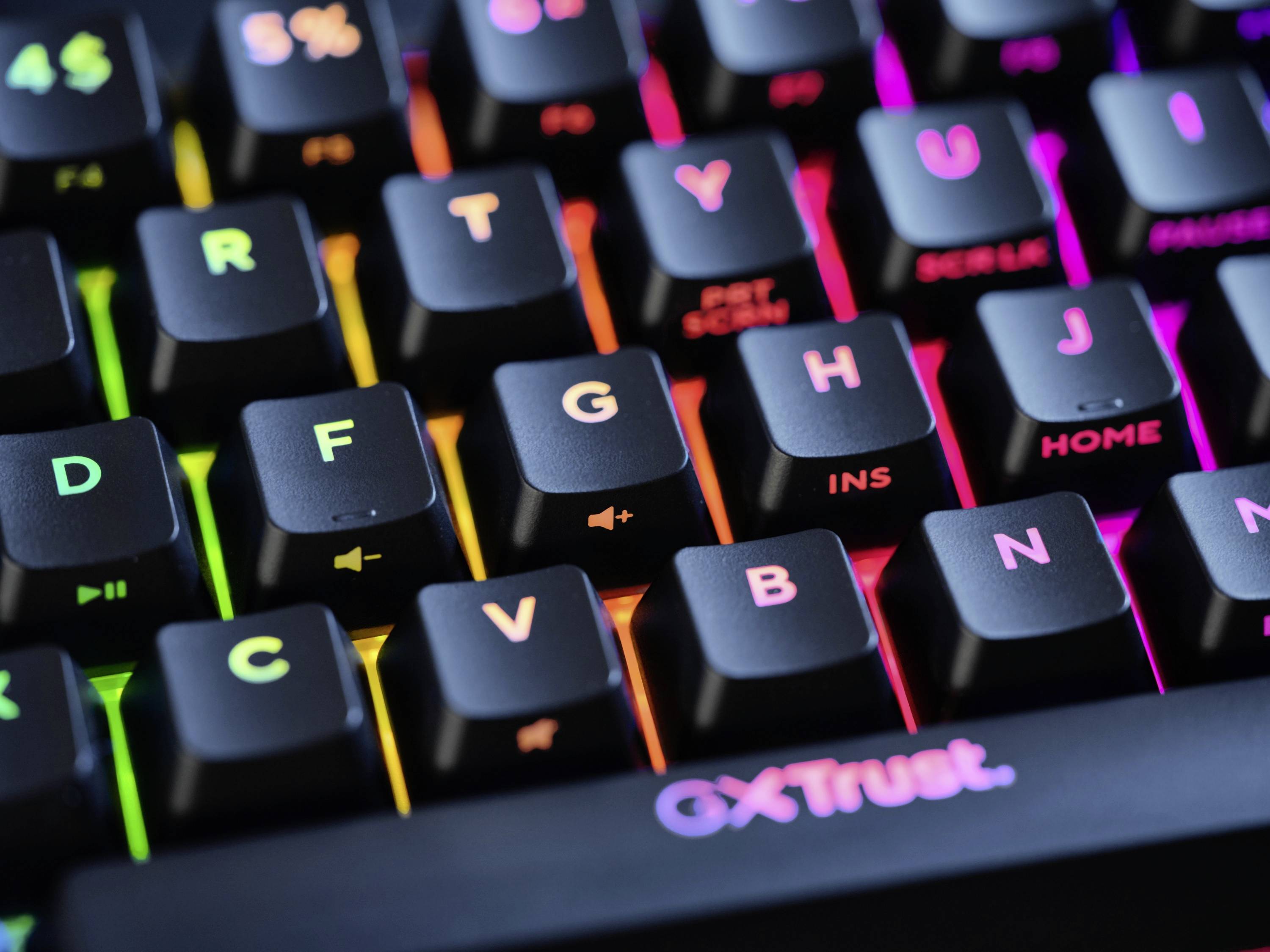 Mechanische Tastatur mit bunten RGB-LEDs, Hintergrundbeleuchtung in verschiedenen Farben, Markenname 'GXTrust' unten sichtbar.