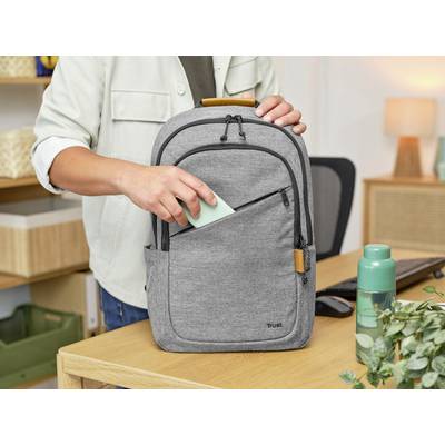 Eine Person steckt eine grüne Notiz in die Vordertasche eines grauen Rucksacks, der auf einem Schreibtisch neben einer Wasserflasche liegt.