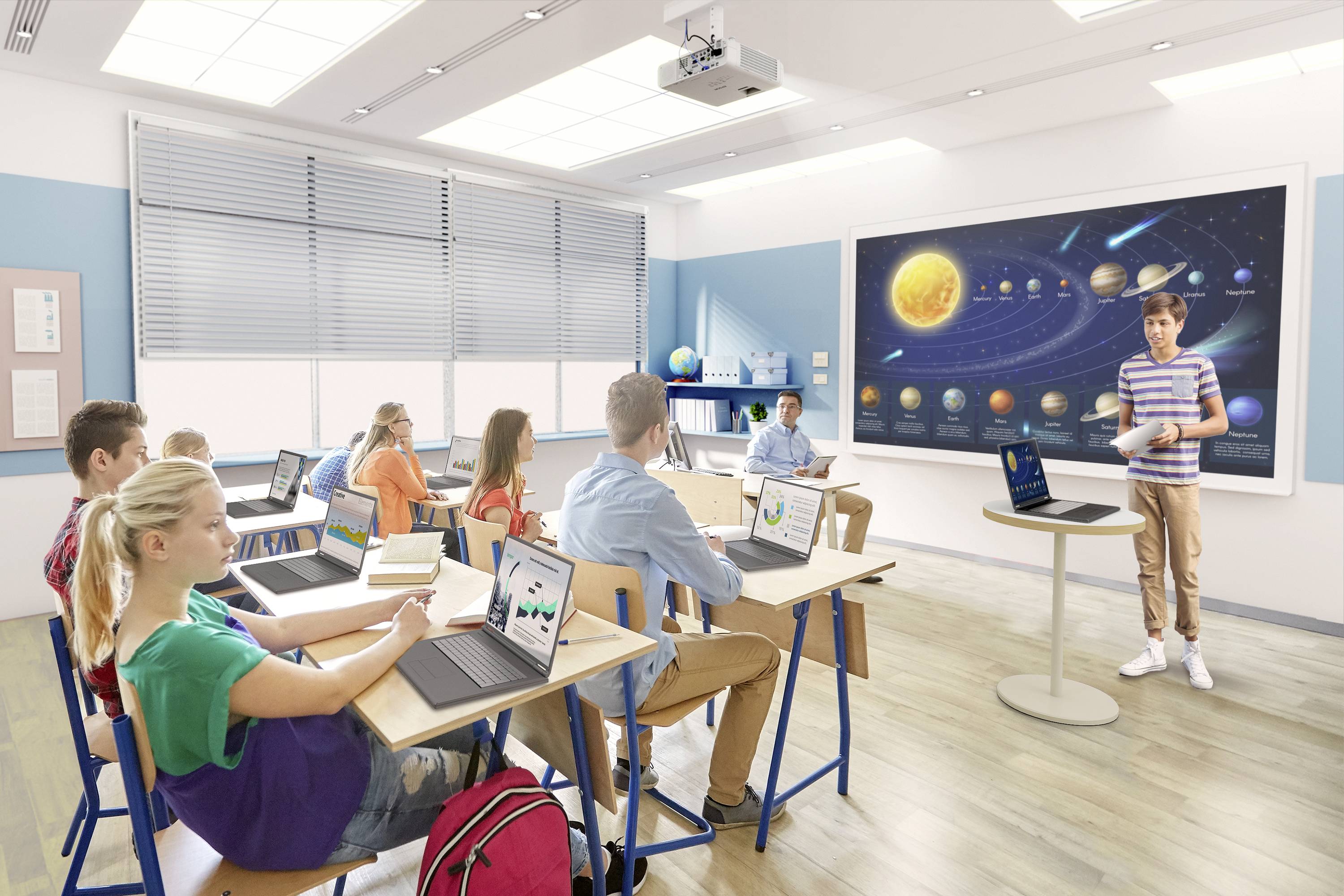 Schüler sitzen in einem Klassenzimmer vor Laptops, während ein Lehrer vor einem Smartboard mit einem Sonnensystem-Diagramm unterrichtet.