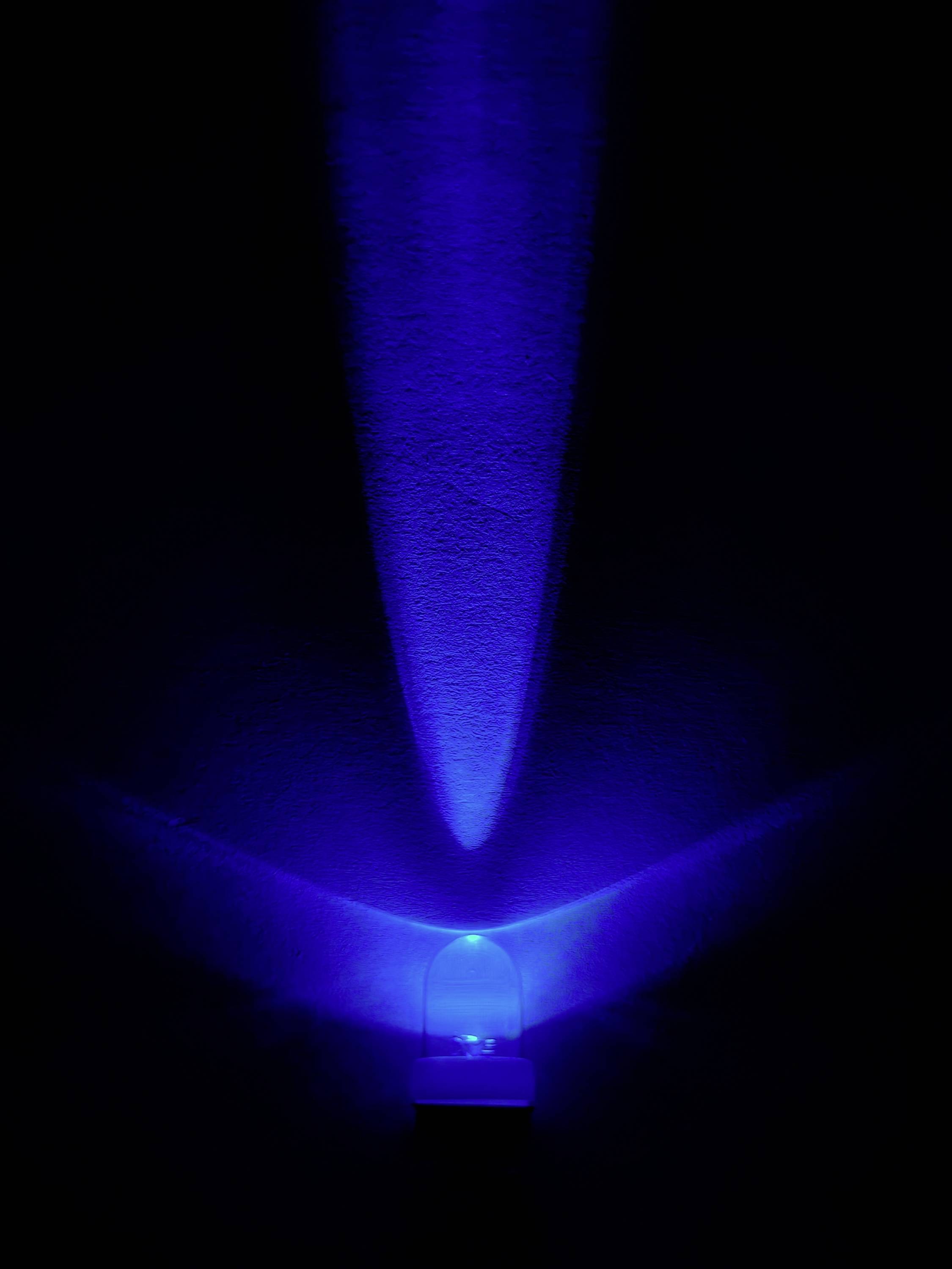 Blaues Licht strahlt von einem kleinen Leuchtobjekt in der Dunkelheit aus und bildet einen strahlenförmigen Muster an der Wand.