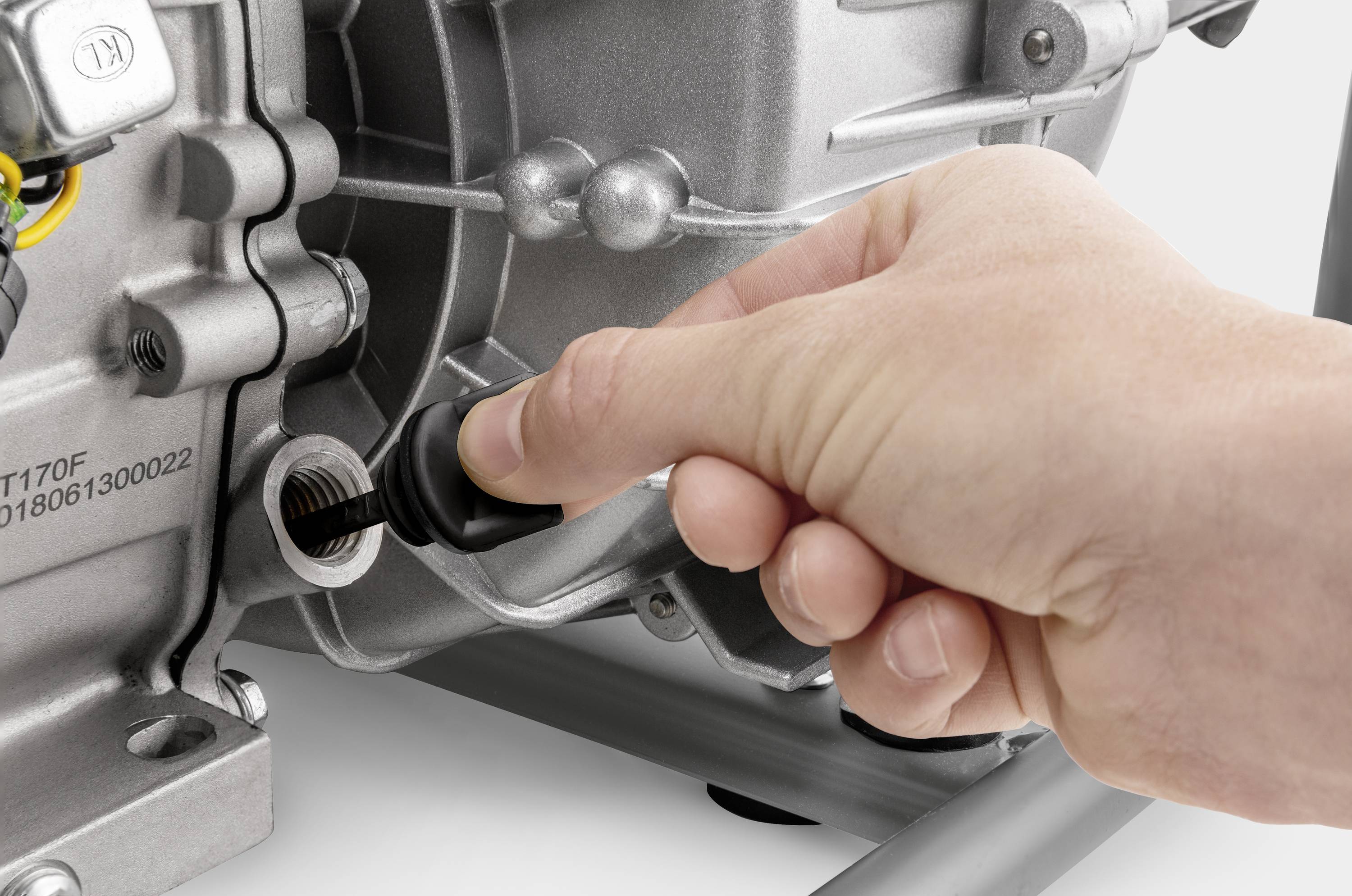 Eine Hand dreht einen Ölmessstab eines Motors heraus. Der Motor ist silberfarben und zeigt technische Details.
