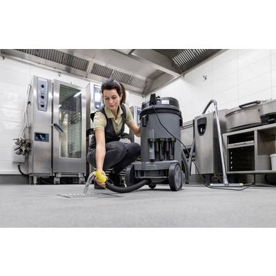 Eine Person verwendet einen Industriesauger, um den Boden in einer professionellen Küche zu reinigen. Im Hintergrund Küchengeräte.