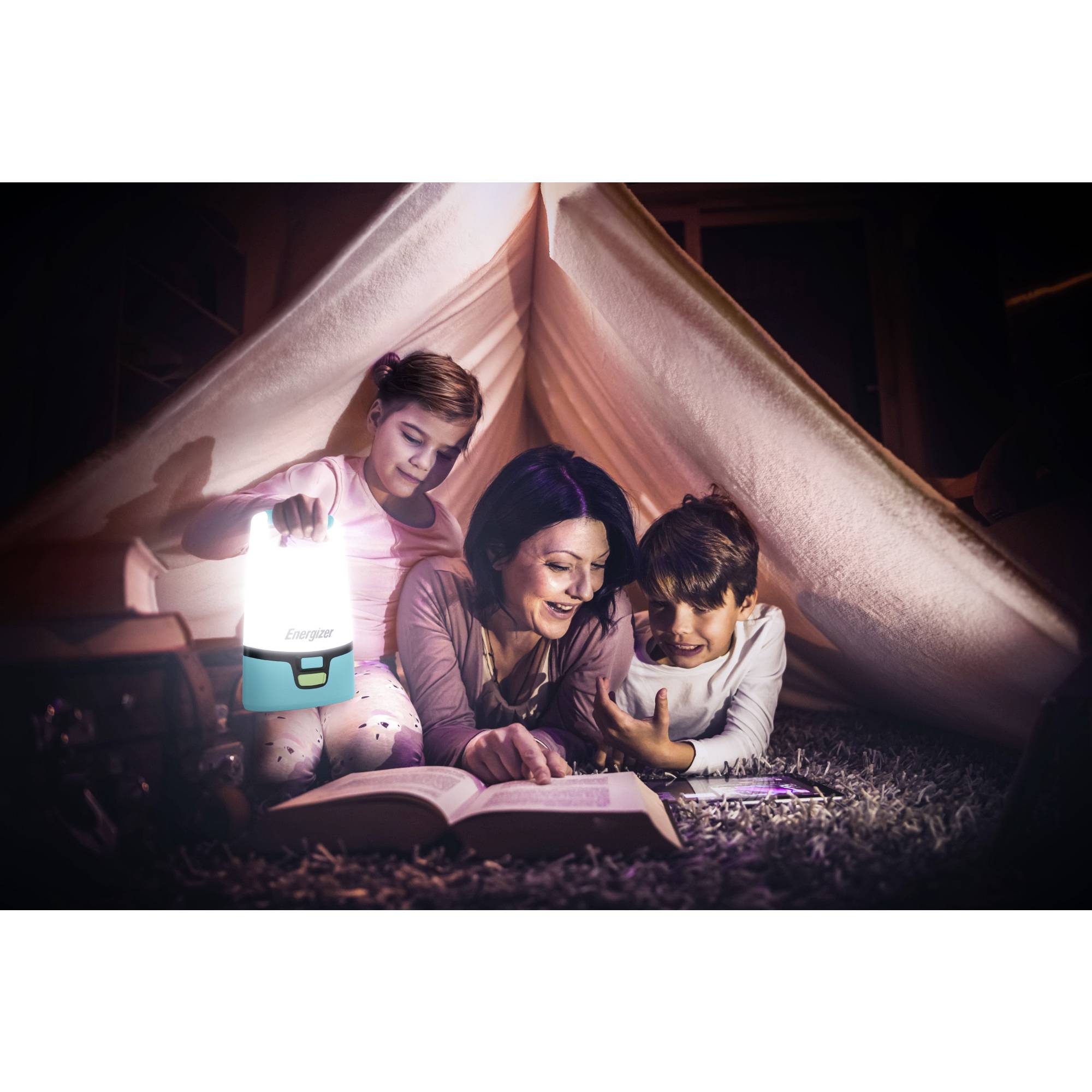 Eine Mutter liest mit ihren beiden Kindern unter einer Decke ein Buch. Ein Kind hält eine leuchtende Laterne, die den Raum erhellt.