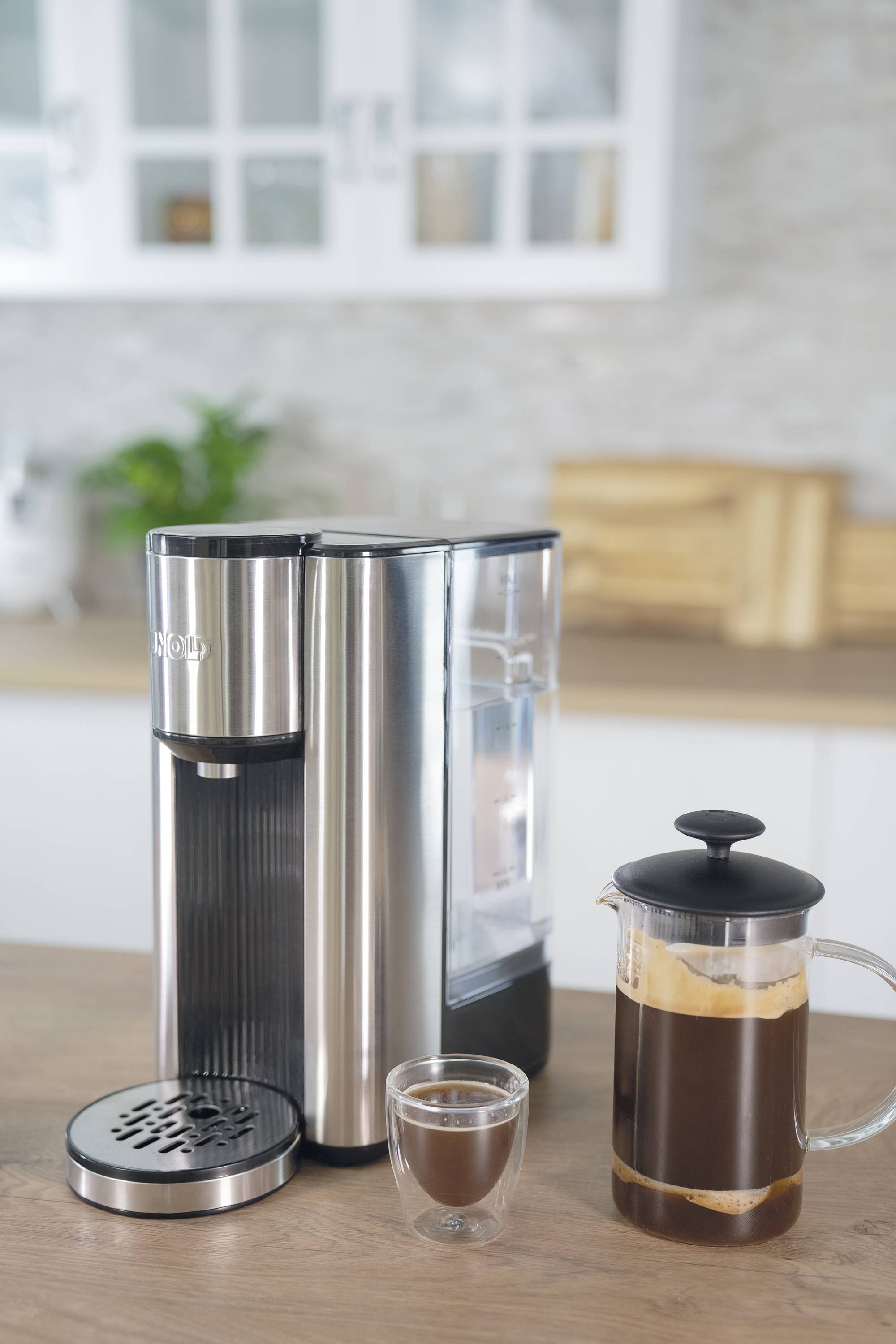 Kaffeemaschine aus Edelstahl auf Küchentheke, daneben eine volle Kanne gebrühter Kaffee und ein gefülltes Glas.